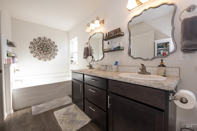 bathroom with double vanity, a garden tub, a sink, and wood finished floors