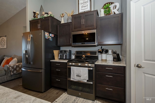 kitchen with appliances with stainless steel finishes, open floor plan, dark brown cabinetry, and wood finished floors