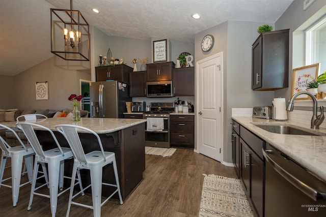 kitchen with light stone counters, a breakfast bar area, appliances with stainless steel finishes, dark brown cabinetry, and a sink