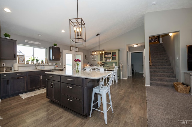 kitchen with lofted ceiling, a sink, a kitchen island, dark brown cabinets, and a kitchen bar