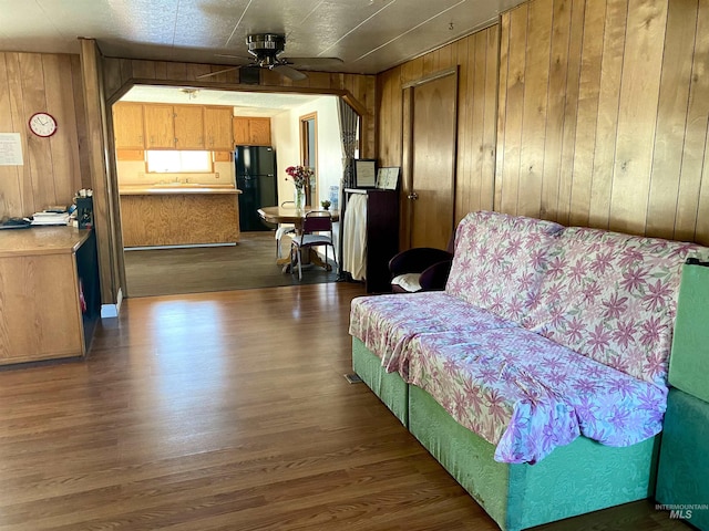 living area featuring wooden walls, ceiling fan, and wood-type flooring