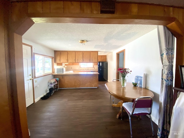 kitchen featuring a textured ceiling, kitchen peninsula, black fridge, and dark hardwood / wood-style floors