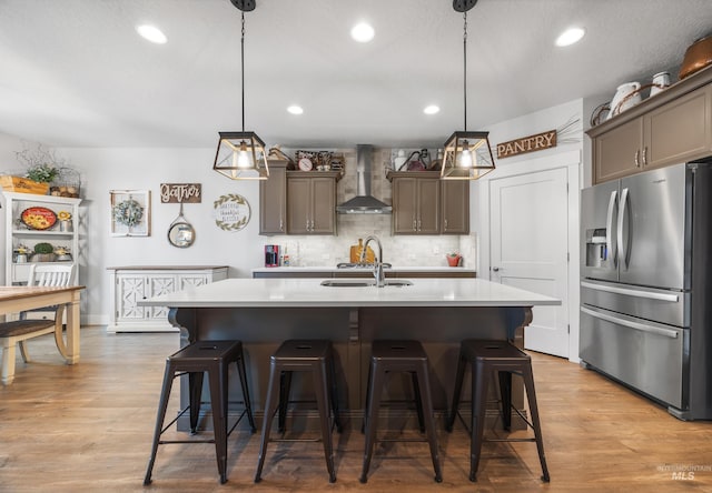 kitchen with a sink, light countertops, stainless steel refrigerator with ice dispenser, wall chimney range hood, and tasteful backsplash