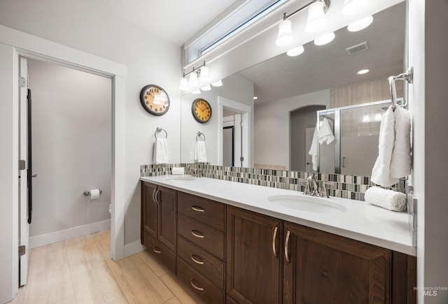 full bath featuring tasteful backsplash, a shower stall, double vanity, and a sink