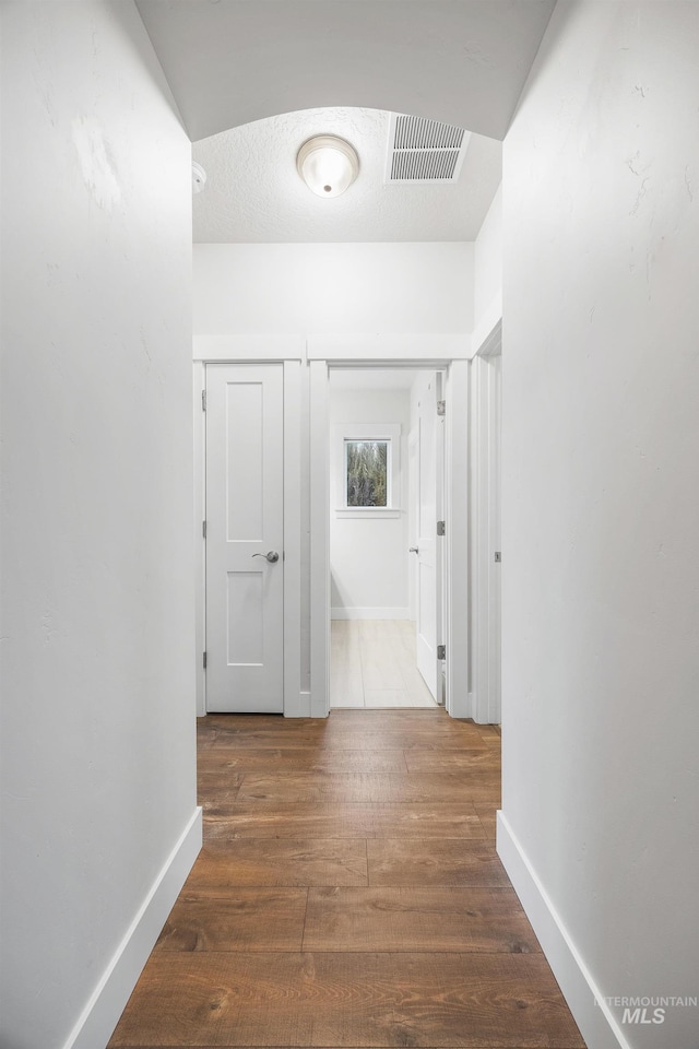 hall featuring a textured ceiling, wood finished floors, visible vents, and baseboards