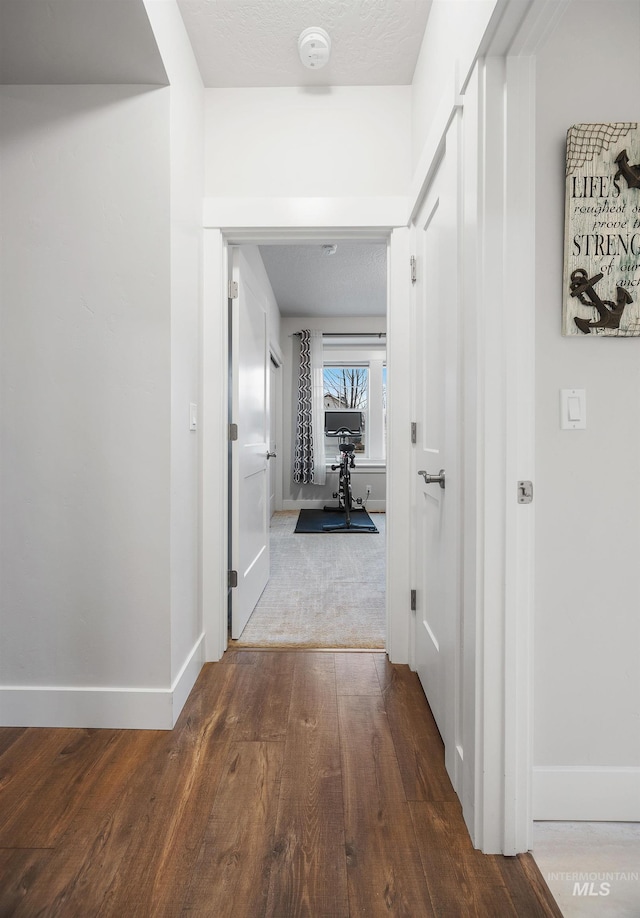 hall featuring wood finished floors, baseboards, and a textured ceiling