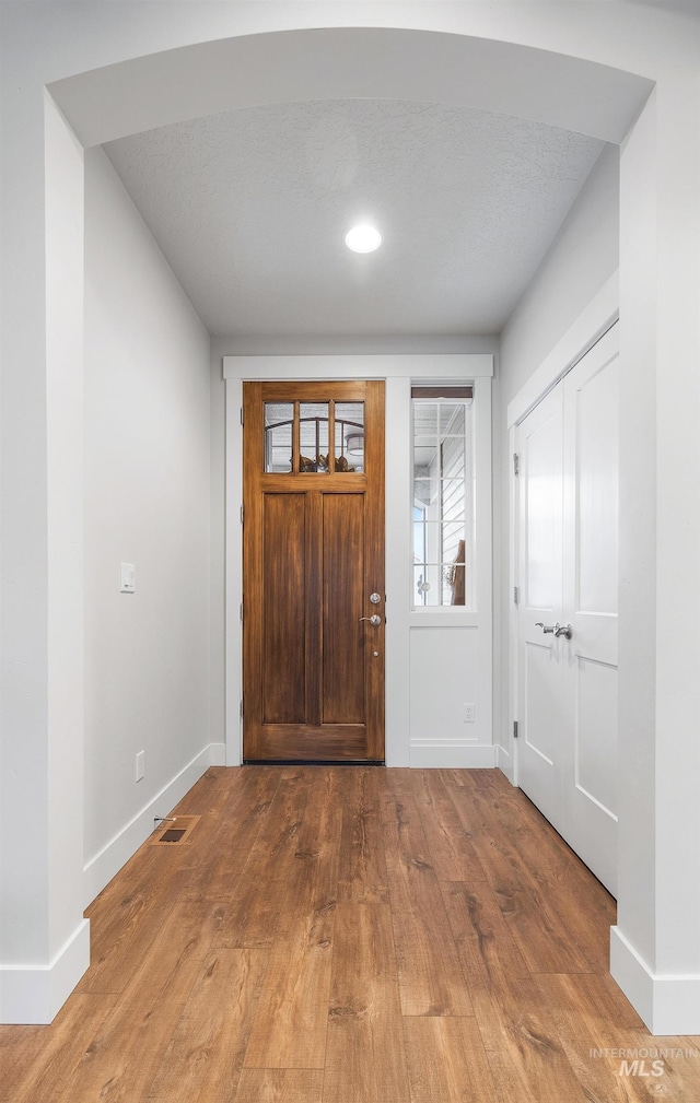 foyer entrance featuring visible vents, baseboards, and wood finished floors