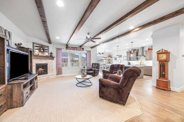 living room with beam ceiling, a textured ceiling, a stone fireplace, baseboards, and ceiling fan