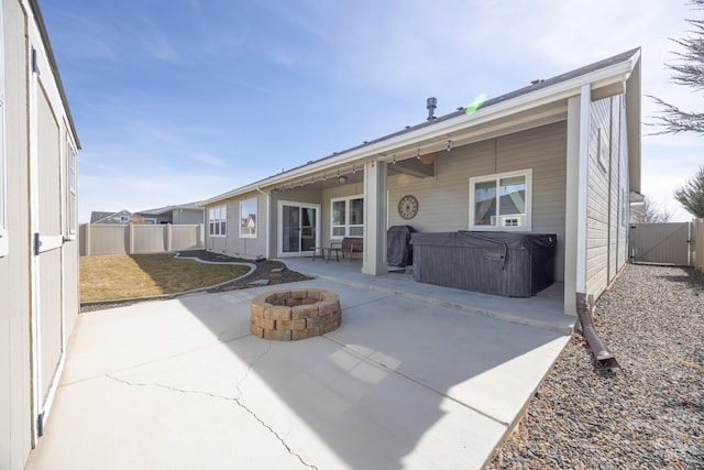 rear view of house with a hot tub, an outdoor fire pit, a fenced backyard, a patio area, and a gate