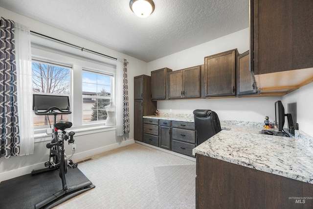 kitchen with a textured ceiling, light stone countertops, dark brown cabinetry, baseboards, and built in study area