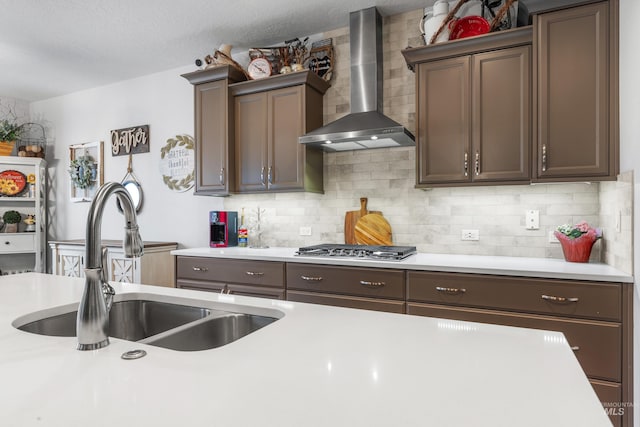 kitchen with stainless steel gas stovetop, light countertops, wall chimney range hood, and a sink