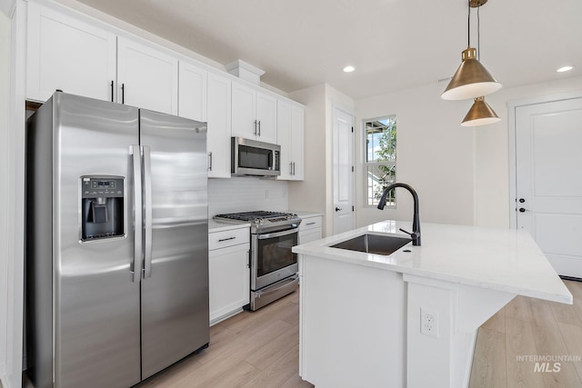 kitchen featuring hanging light fixtures, appliances with stainless steel finishes, a kitchen island with sink, a sink, and white cabinetry