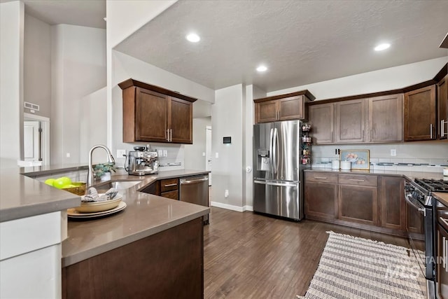 kitchen with stainless steel appliances, recessed lighting, dark wood-type flooring, a sink, and dark brown cabinets