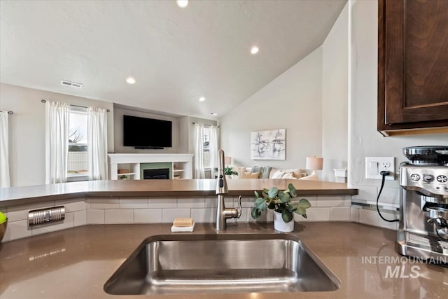 kitchen featuring a fireplace, visible vents, open floor plan, vaulted ceiling, and a sink