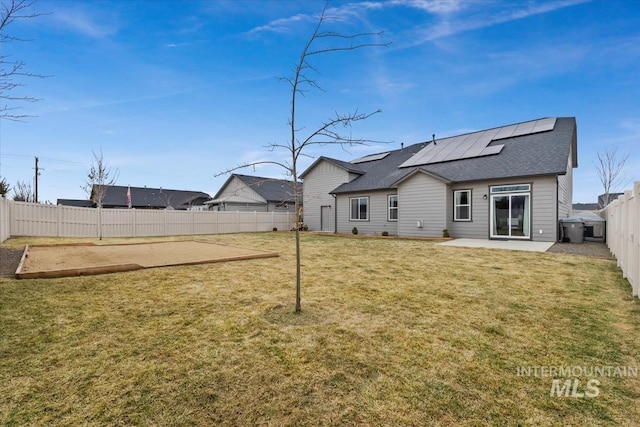 rear view of house with a yard, a patio, solar panels, a shingled roof, and a fenced backyard