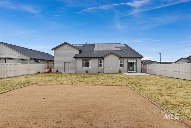 back of property with a fenced backyard, a shingled roof, a yard, roof mounted solar panels, and a patio area