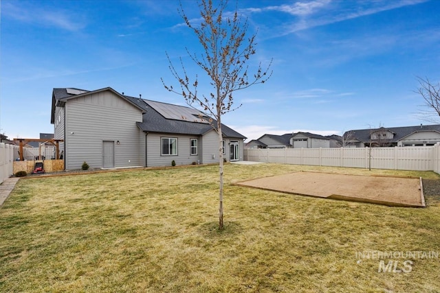 back of house with a yard, a fenced backyard, roof mounted solar panels, and a patio