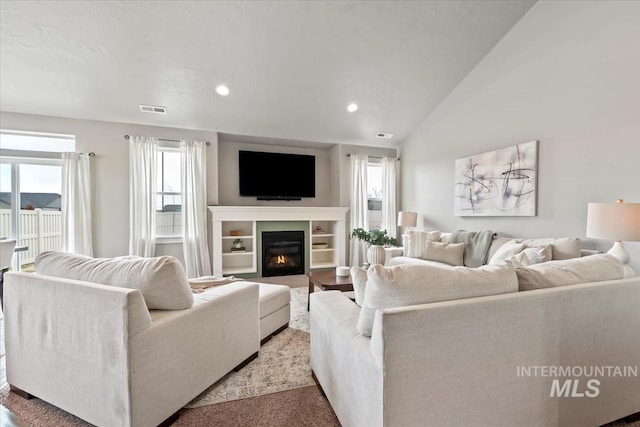 living room featuring lofted ceiling, visible vents, a glass covered fireplace, and recessed lighting