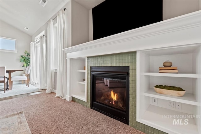 room details with a tiled fireplace, carpet flooring, visible vents, and built in features