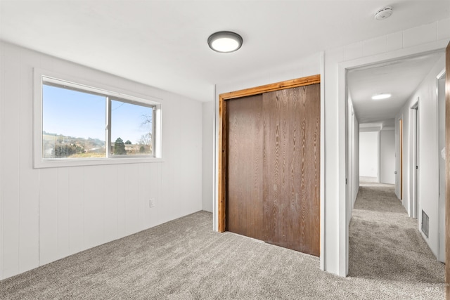 unfurnished bedroom with carpet, wooden walls, and a closet