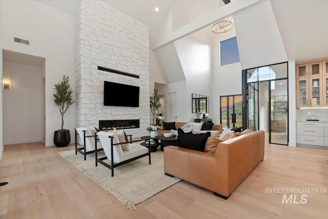 6162 N High Valley Way, Boise, ID 83714 - living room with a high ceiling, light wood-style flooring, a stone fireplace, a chandelier, and baseboards