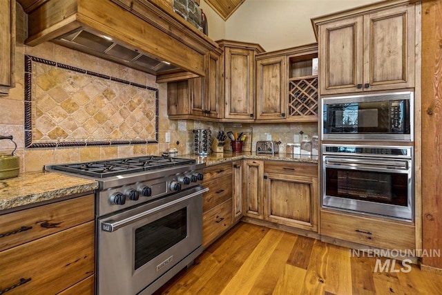 516 Whitewater Dr, Donnelly, ID 83615 - kitchen with light stone counters, appliances with stainless steel finishes, light hardwood / wood-style flooring, backsplash, and custom exhaust hood