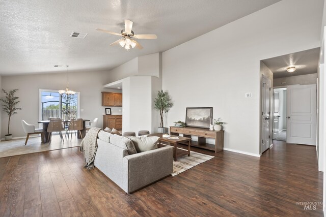 living area with visible vents, ceiling fan with notable chandelier, dark wood-type flooring, and lofted ceiling