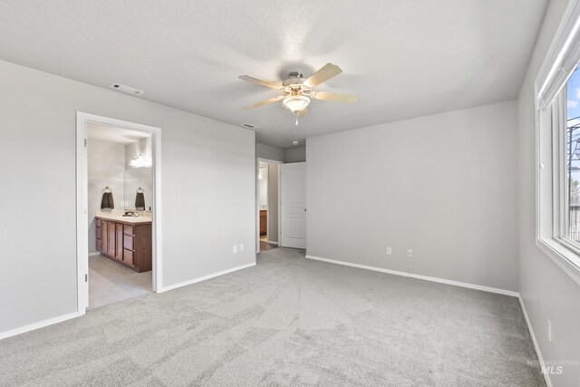 unfurnished bedroom featuring baseboards, light colored carpet, connected bathroom, and visible vents