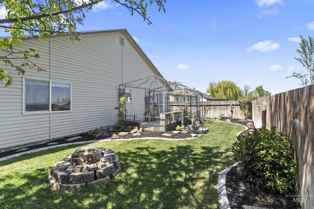 view of side of home featuring a lawn, fence private yard, and an outdoor fire pit