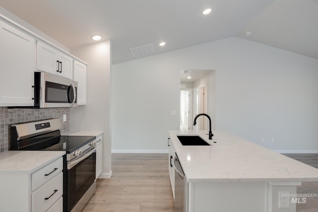 kitchen with appliances with stainless steel finishes, vaulted ceiling, sink, a center island with sink, and white cabinets