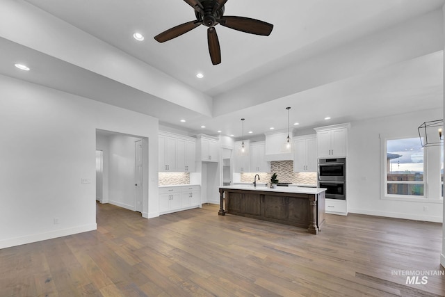 kitchen with decorative light fixtures, a kitchen bar, white cabinetry, double oven, and a kitchen island with sink