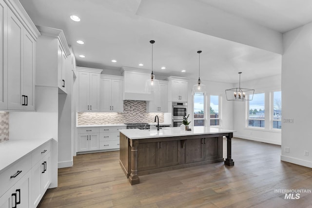 kitchen with a breakfast bar area, pendant lighting, white cabinets, and an island with sink