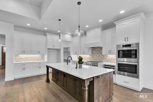 kitchen with a center island with sink, appliances with stainless steel finishes, pendant lighting, and white cabinets