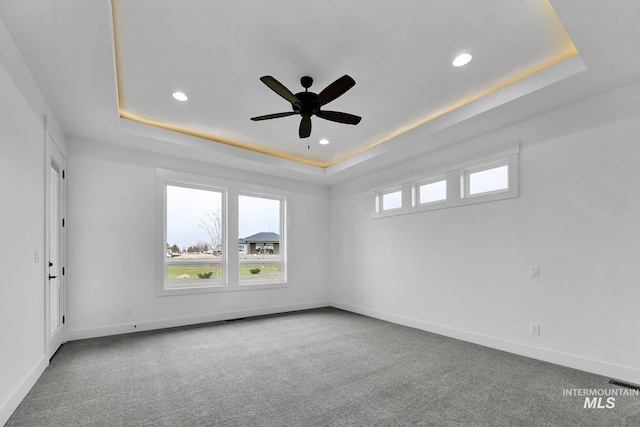 carpeted empty room with ceiling fan and a tray ceiling