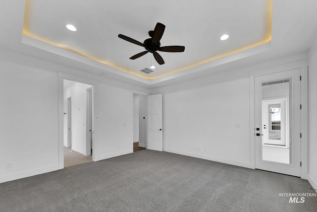 empty room featuring ceiling fan, carpet flooring, and a tray ceiling