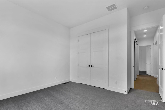 unfurnished bedroom with dark colored carpet, a closet, and a barn door