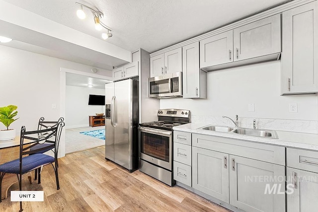 kitchen featuring gray cabinets, appliances with stainless steel finishes, light wood-type flooring, a textured ceiling, and sink