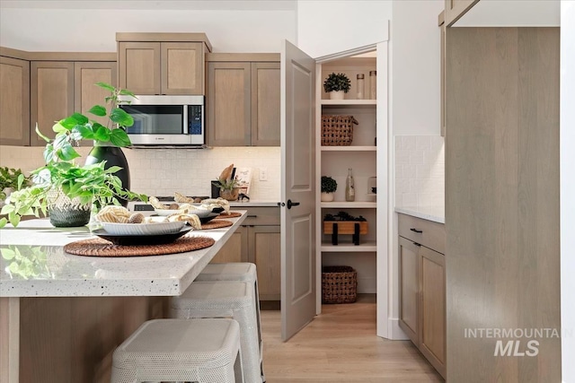 kitchen featuring light stone counters, decorative backsplash, light hardwood / wood-style flooring, and a breakfast bar