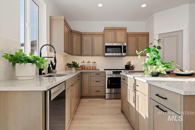 kitchen featuring tasteful backsplash, sink, light hardwood / wood-style flooring, and appliances with stainless steel finishes