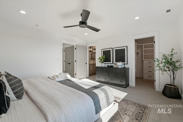 bedroom with ceiling fan, connected bathroom, a walk in closet, light colored carpet, and a closet