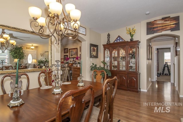 dining room with arched walkways, wood finished floors, a chandelier, and baseboards