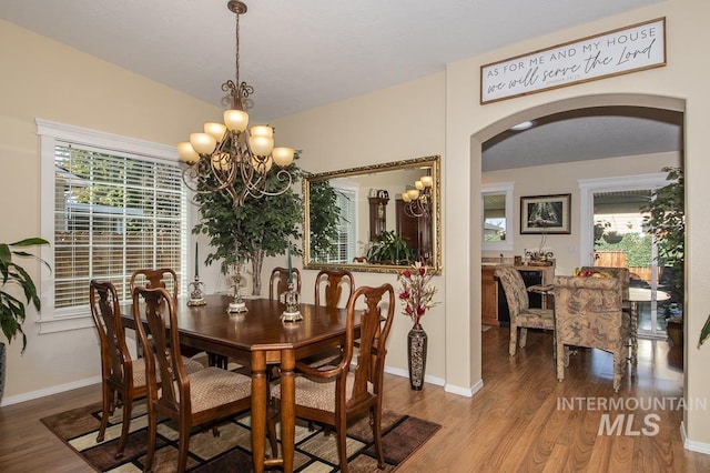 dining space featuring arched walkways, wood finished floors, a chandelier, and plenty of natural light