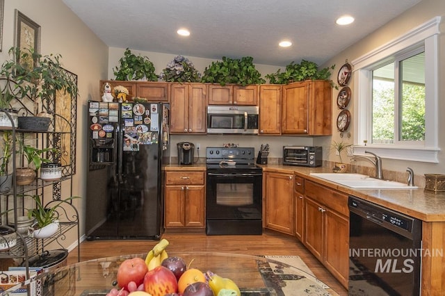 kitchen with black appliances, a sink, light wood-style floors, brown cabinets, and recessed lighting