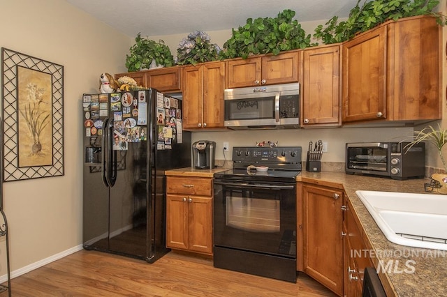 kitchen featuring black appliances, light wood finished floors, brown cabinetry, a sink, and light countertops