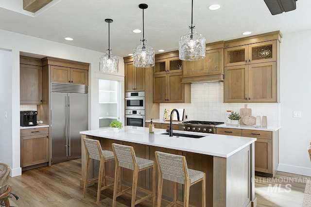 3389 E Englehart Dr, Meridian, ID 83642 - kitchen with stainless steel appliances, brown cabinetry, light wood-style floors, backsplash, and a center island with sink