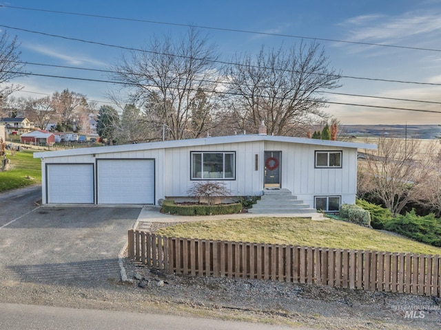 view of front facade featuring driveway, fence, board and batten siding, a front yard, and an attached garage