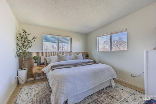 bedroom with vaulted ceiling, baseboards, light wood-type flooring, and a textured ceiling