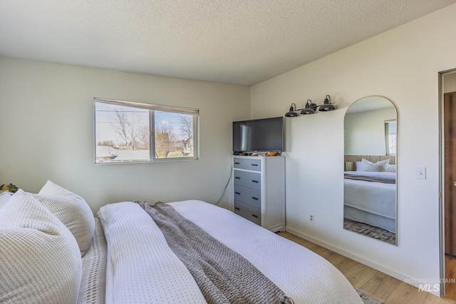 bedroom with baseboards, arched walkways, light wood-type flooring, and a textured ceiling