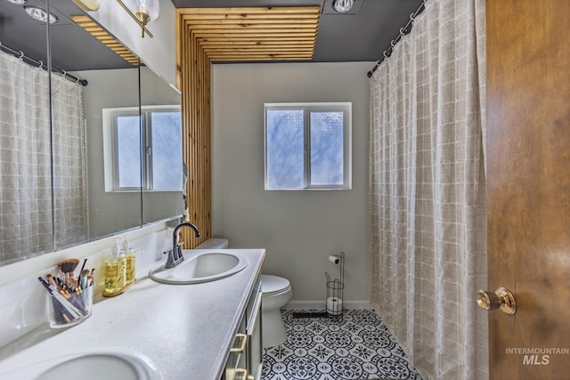 bathroom featuring toilet, a sink, tile patterned flooring, double vanity, and baseboards