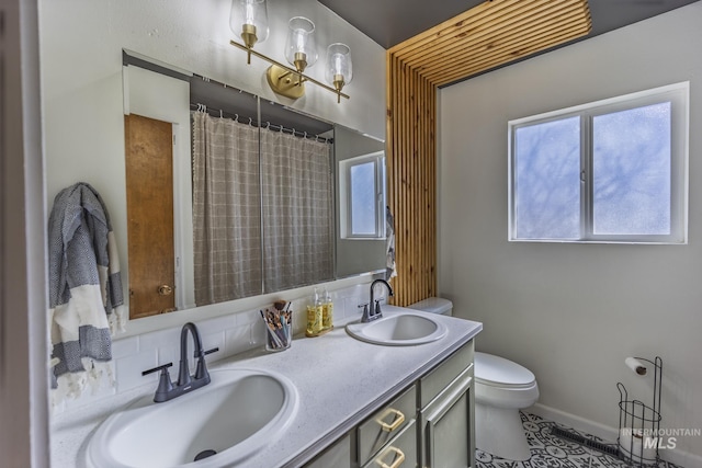 bathroom with double vanity, toilet, baseboards, and a sink